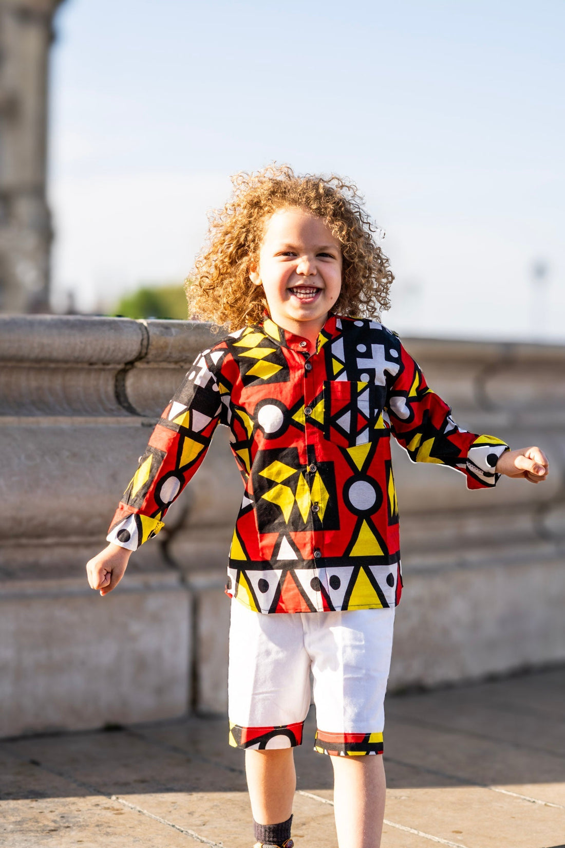 etit garçon portant une chemise en wax et un bermuda, illustration de l’origine et de l’utilisation du tissu wax dans la mode enfant.