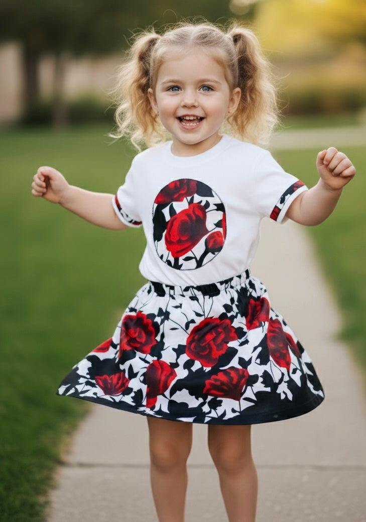 Fillette souriante portant un t-shirt blanc customisé avec un motif en tissu wax coloré, assorti à une jupe évasée en wax aux tons vifs. Tenue joyeuse et moderne mêlant style urbain et influences africaines.