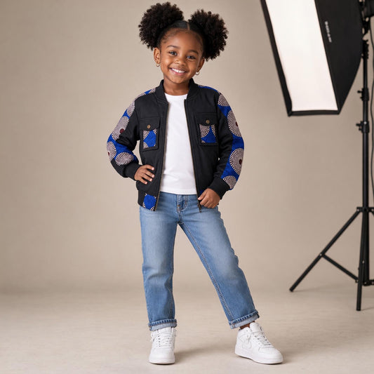 Fille portant une veste bomber MBEMA noire avec manches et détails de poches en wax bleu, blanc et bordeaux, associée à un jean