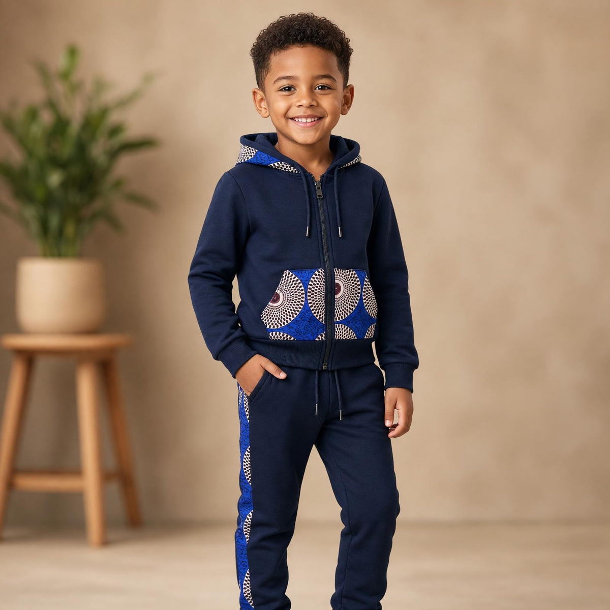 Enfant portant un ensemble jogging MBEMA bleu marine avec veste à capuche zippée et détails en wax bleu, blanc et bordeaux sur les poches et le pantalon.