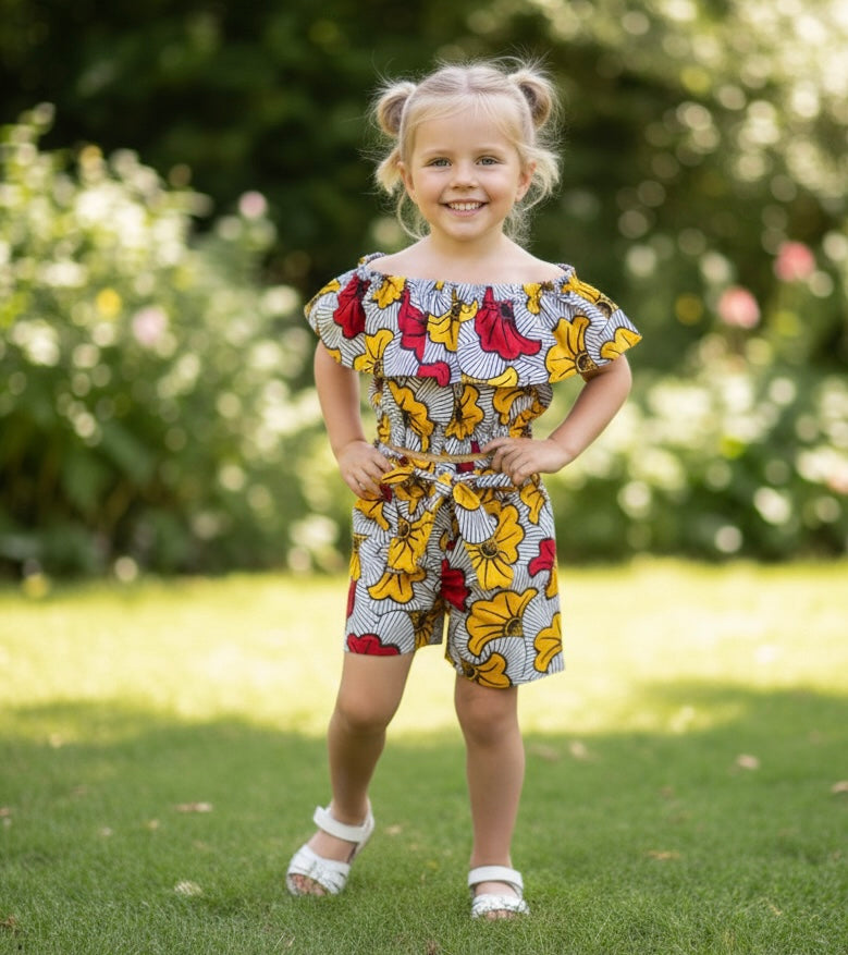 Vue en plein pied d’une petite fille habillée en wax, avec un ensemble deux pièces : crop top à volants et short à fleurs, parfait pour les événements festifs ou l’été.