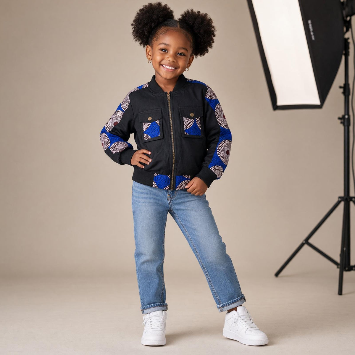 Veste aviateur fille MBEMA noire à fermeture zippée, avec motifs wax bleus, blancs et bordeaux sur les manches, les poches et le bas.